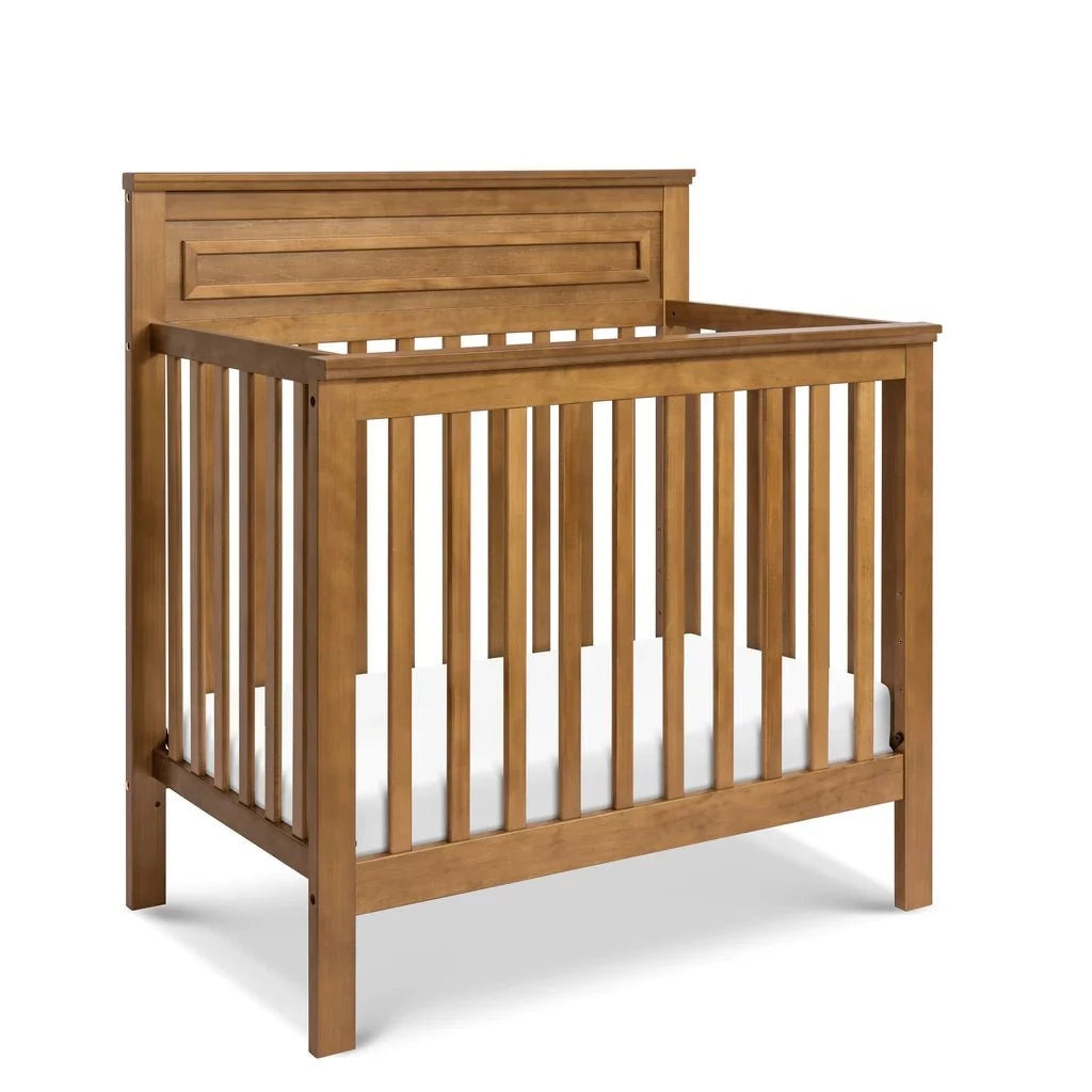Wooden crib with vertical slats and a simple, clean design, featuring a neutral light wood finish and a white mattress.