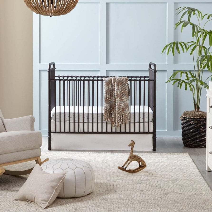 Black metal convertible crib styled in a cozy Canadian nursery with neutral decor and wooden giraffe rocker.
