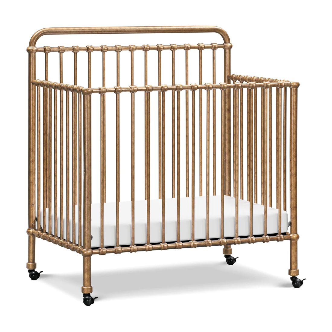 Gold-finished metal crib with vertical bars and a white mattress, featuring caster wheels for easy mobility.